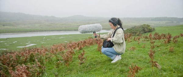 A professional sound mixer using a shotgun microphone to capture an ambient field recording. 