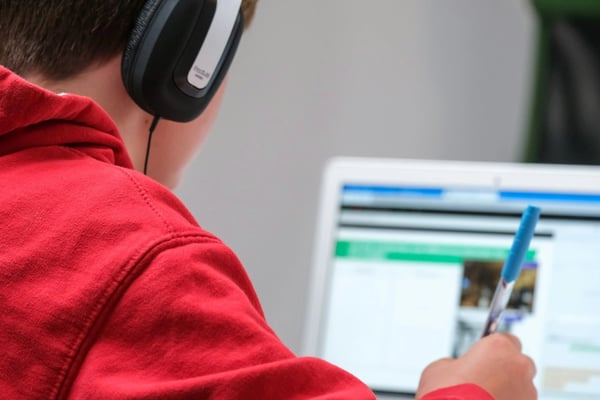 Close-up of student in red jacket and headphones working on laptop.