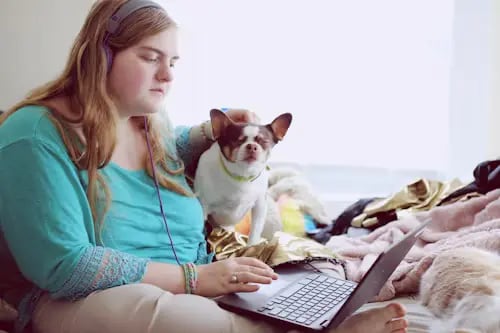 A young woman completes school work at home with her dog by her side, using the flipped classroom model.