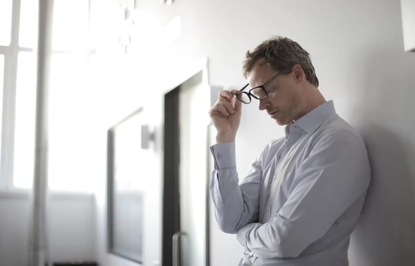 A teacher leaning against wall and taking off glasses.