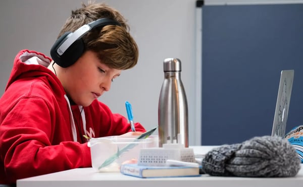 Boy with red and white hoodie at laptop wearing black headphones.