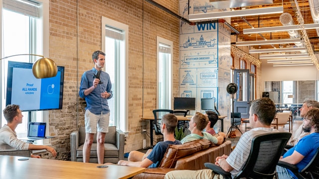 Man presenting all-hands meeting deck to co-works in trendy workspace. 