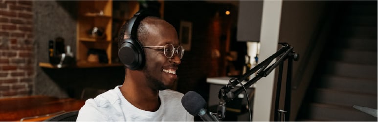Black man smiling with headphones speaking into podcast mic - smaller