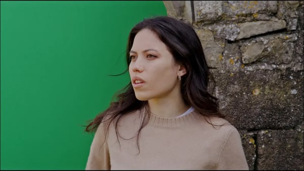 Brunette woman in brown sweater showing half green screen backdrop and half brown brick.