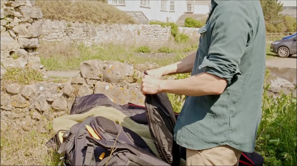 Man in green shirt and khakis taking out a portable green screen set from his backpack outside.