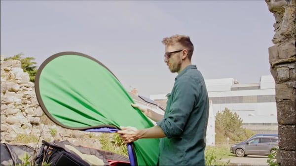 Blonde man expanding portable green screen outside.