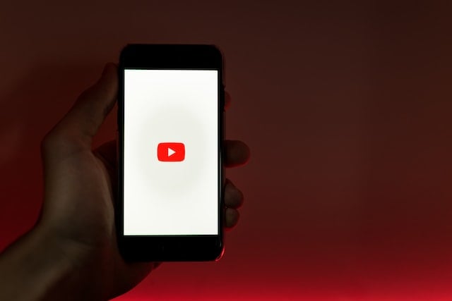 Hand holding YouTube video on iPhone, set against red background
