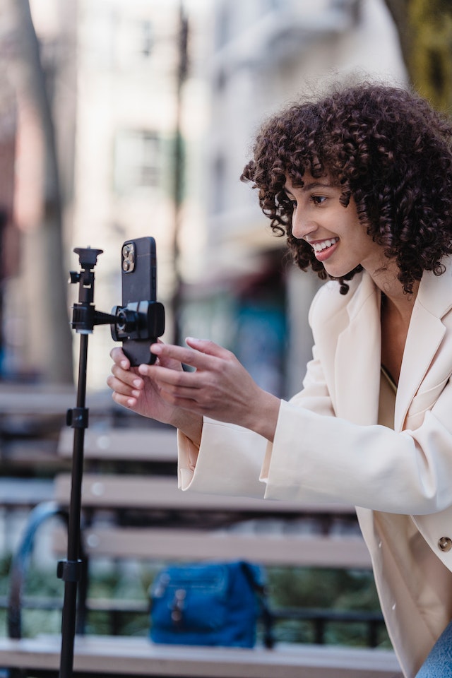 Image of woman in beige coat reaching for her phone camera on a tripod