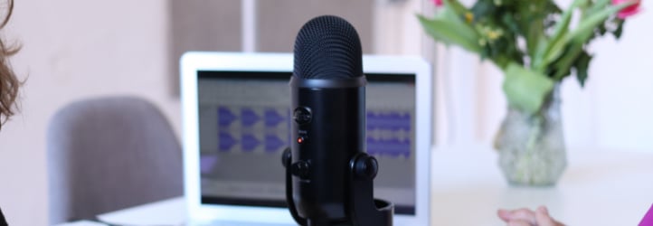 Close-up of podcasting microphone on table. Open laptop behind it.