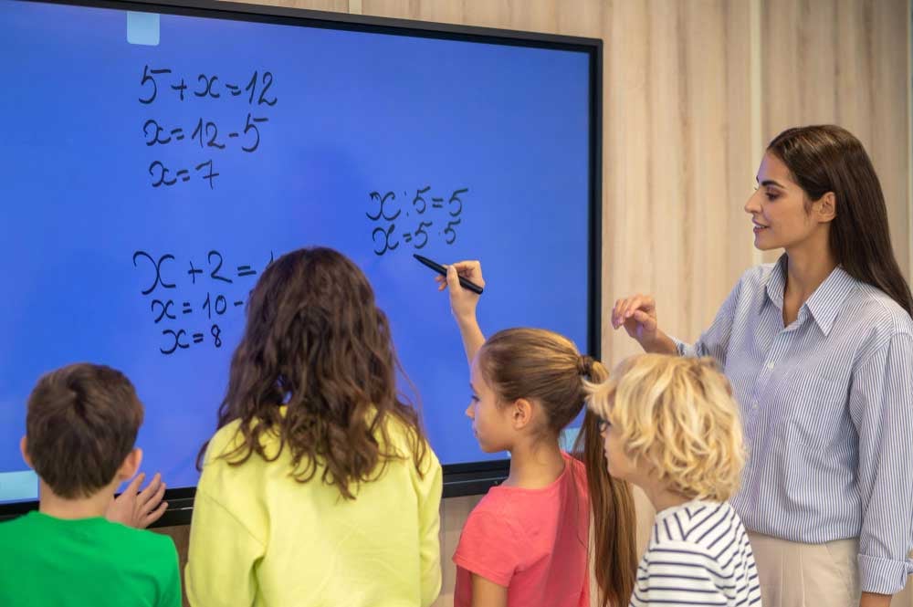 Teacher with group of students working on math problems at digital whiteboard