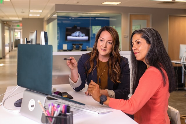 Female manager points at computer while female new hire sits engaged.