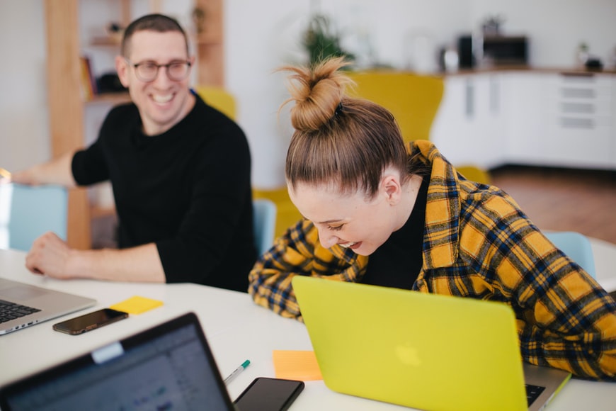 Employee communication in action: Man and woman laughing at work in front of their computers.