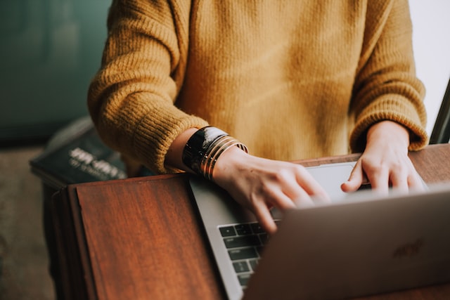 Woman in yellow sweater using laptop on table with only body visible