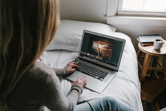 Woman sitting on bed using laptop to create YouTube image sizing