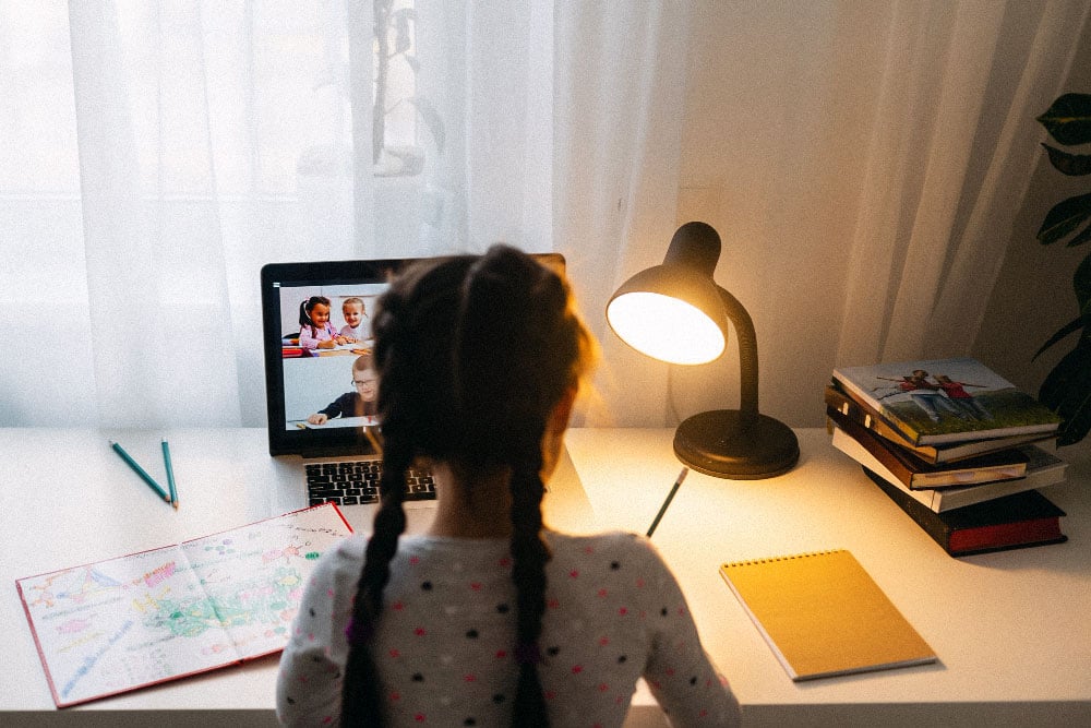 Young girl working on laptop with other students on screen