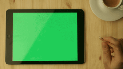A tablet with green background and a hand playing with a pencil