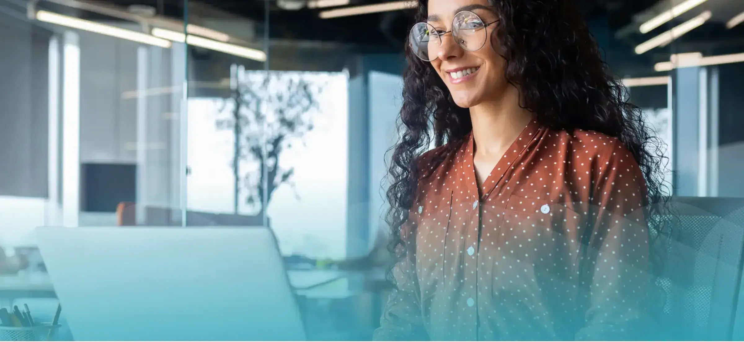 Female learner with glasses and long, curly hair smiling while looking at a laptop.