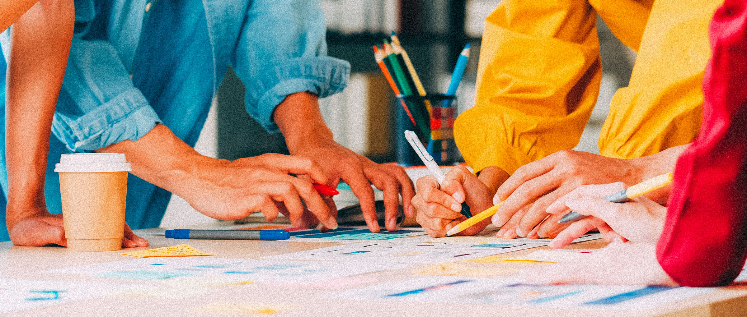 Close-up image of four people working on a creative art project with paper and pencils