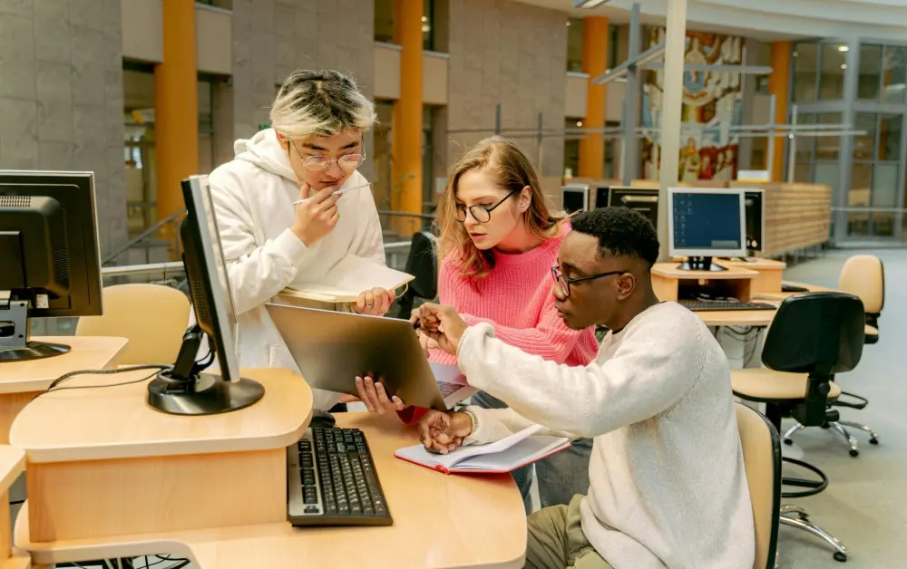 Three higher education students sitting and working together around a computer.