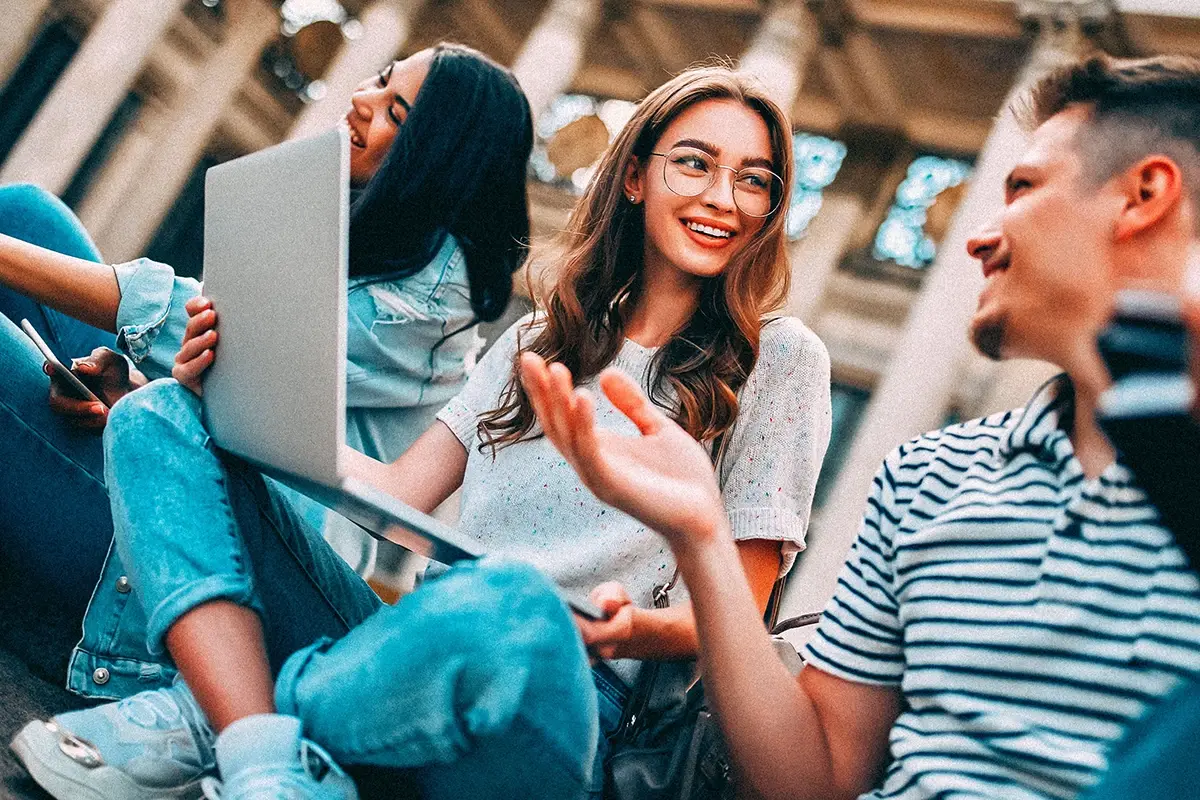 Higher ed students smiling and chatting together behind a laptop
