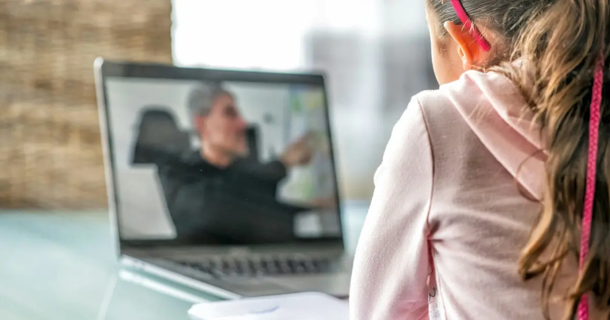 Young female student on computer laptop listening to male teacher and taking notes.