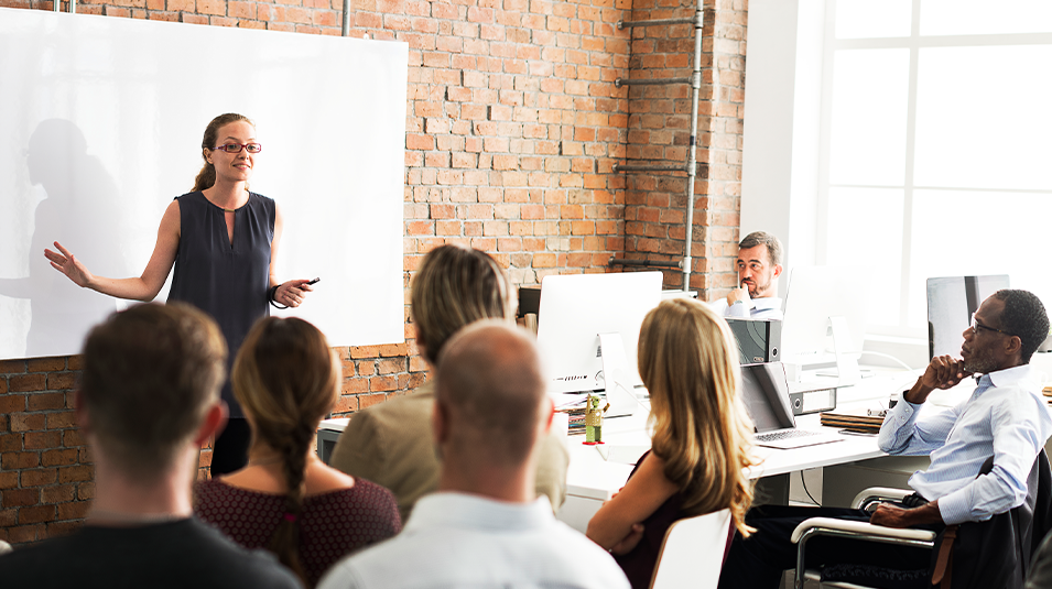 Woman standing in front of large whiteboard and presenting to department.