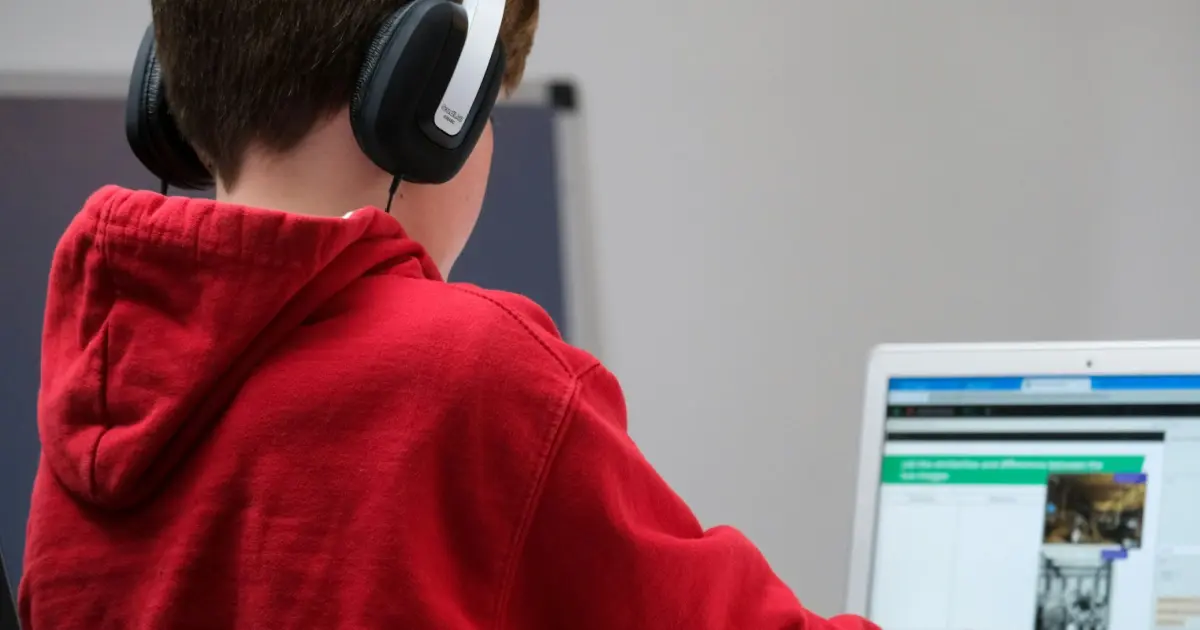 Young male student with headphones and a red sweatshirt doing an assignment on the computer.
