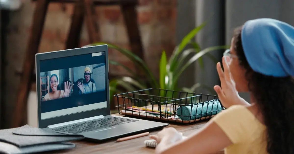 Female student waving to two classmates on computer.