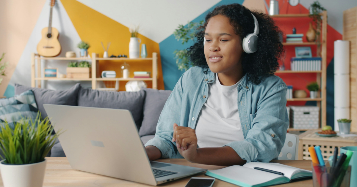 Young student with headphones smiling at computer working on an assignment