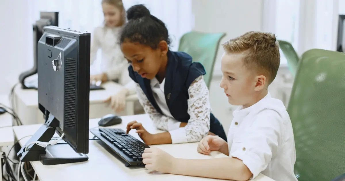 Two young students sitting together typing at a computer.
