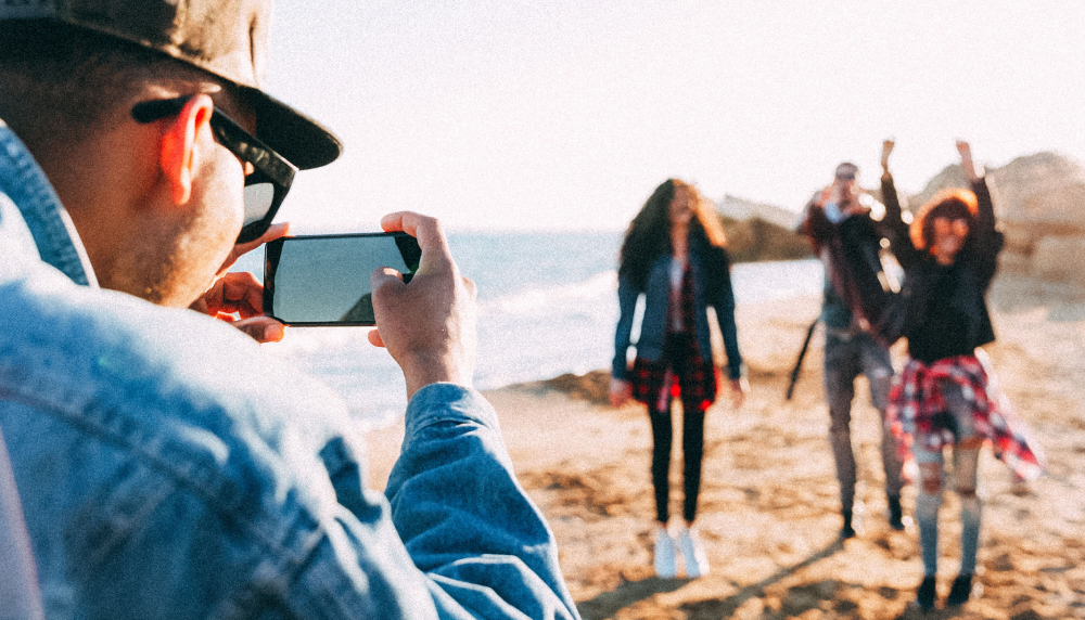 Man filming a video of three friends on a beach using his iPhone