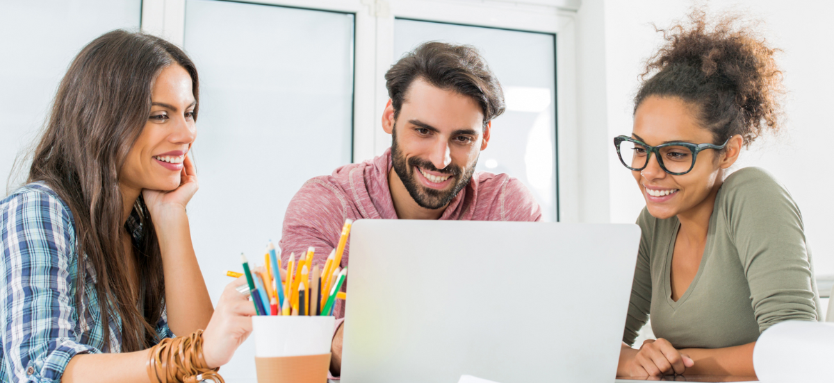 Three learners gathered around a computer (two female, one male) smiling while they work.