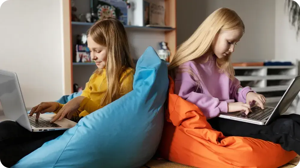 K-12 learners sitting back-to-back on bean bags while they work on laptops.