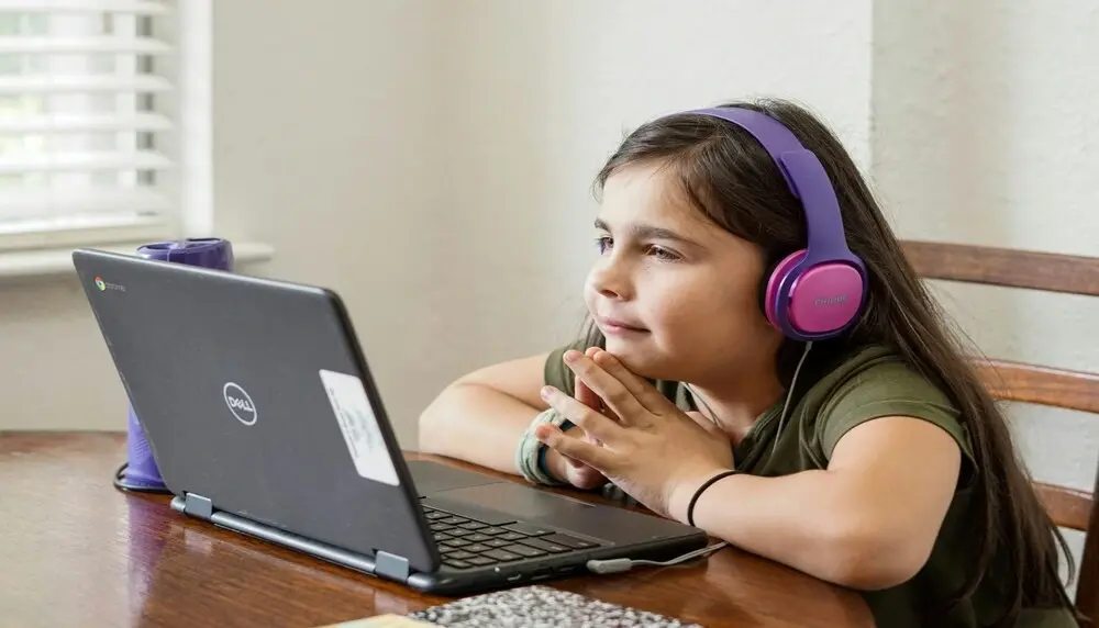 Young female student with pink and purple headphones learning in front of a computer resting her face on her hands