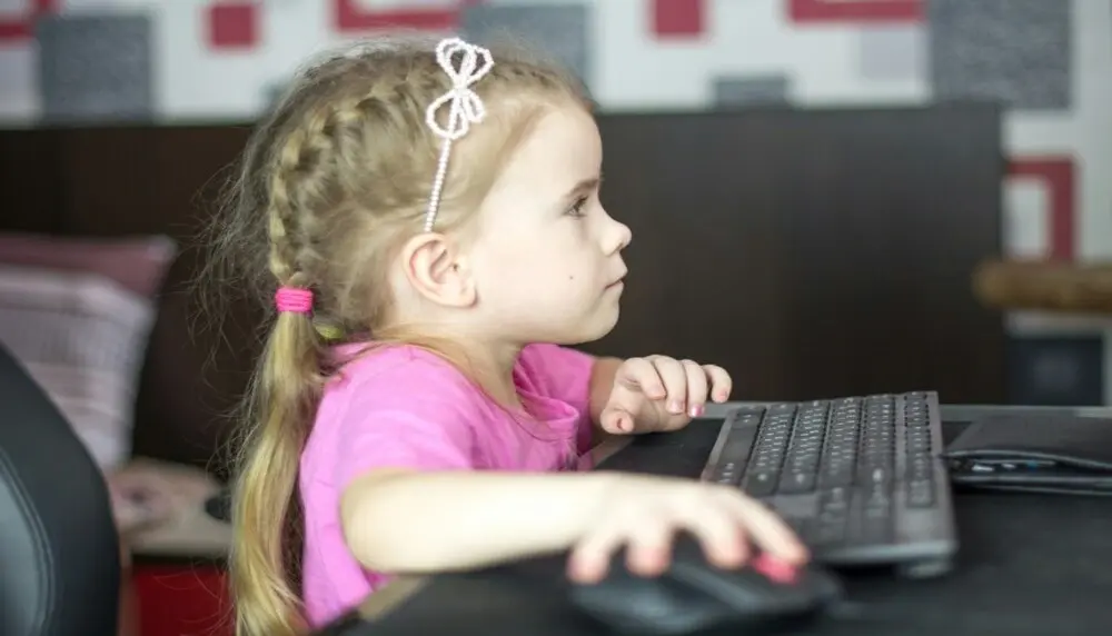 Blonde learner with braids and a pink shirt on working in front of a computer