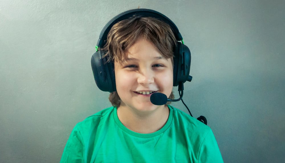 Young student smiling in a green shirt facing the camera wearing a headset.