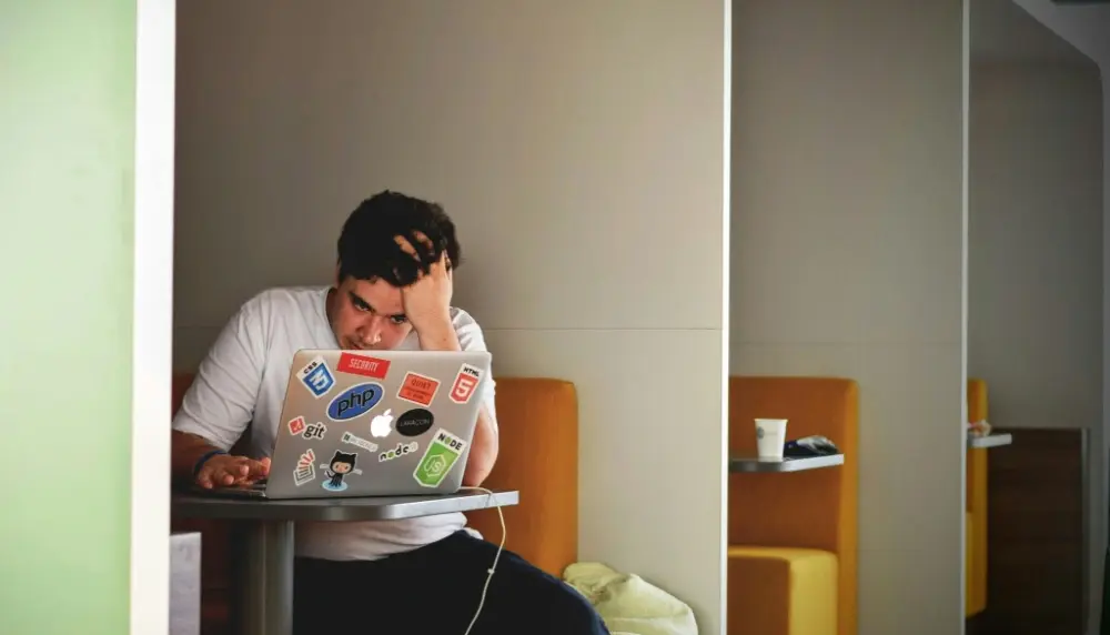 Male college student on a plugged-in laptop with hand on his head in focus mode.