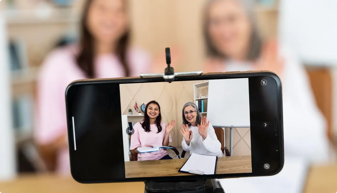 Two women smiling behind a camera as they record a video for school communications