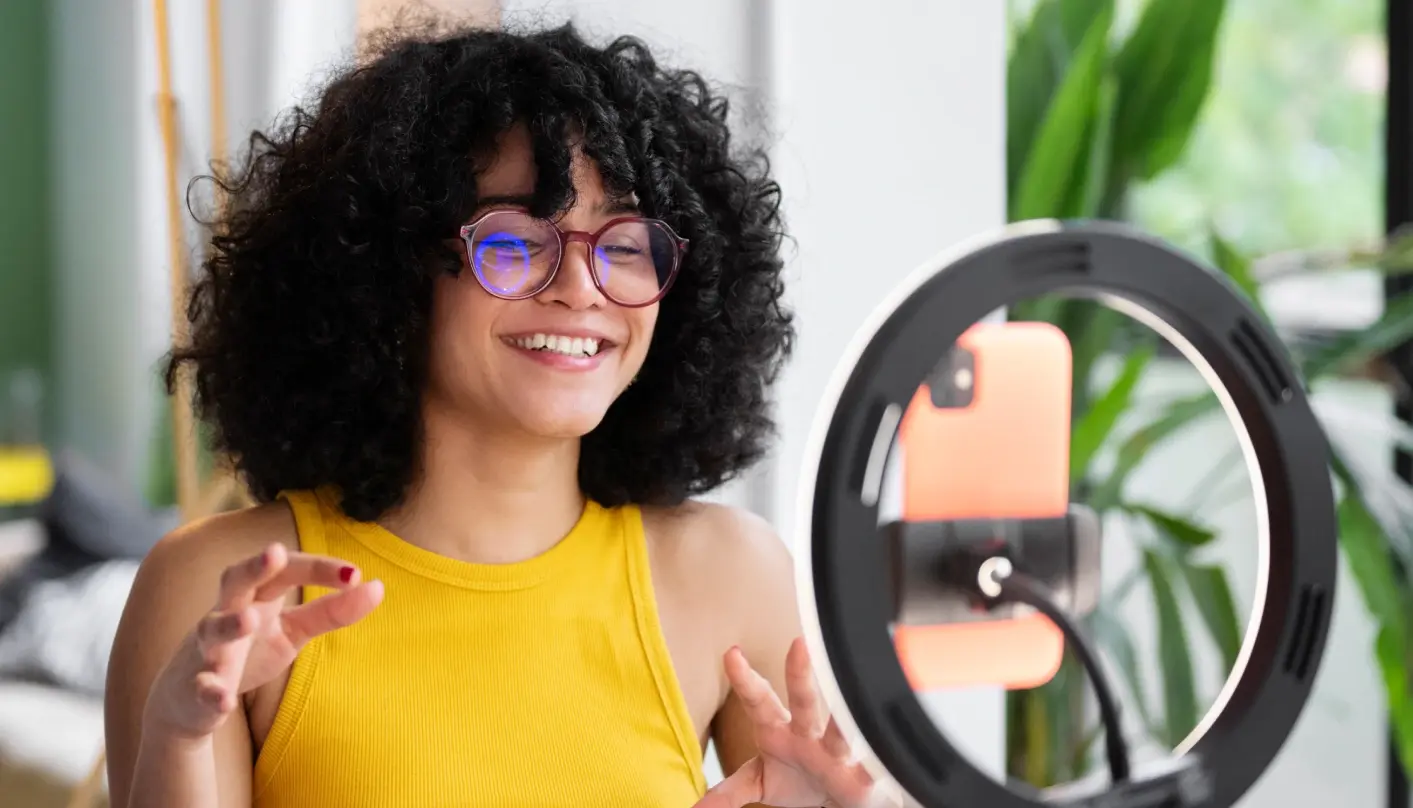 Woman smiling in front of a smartphone and a ring light as she records a video for social media