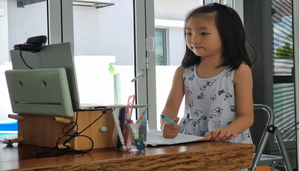 Girl standing up and taking notes in front of a computer with a camera on it