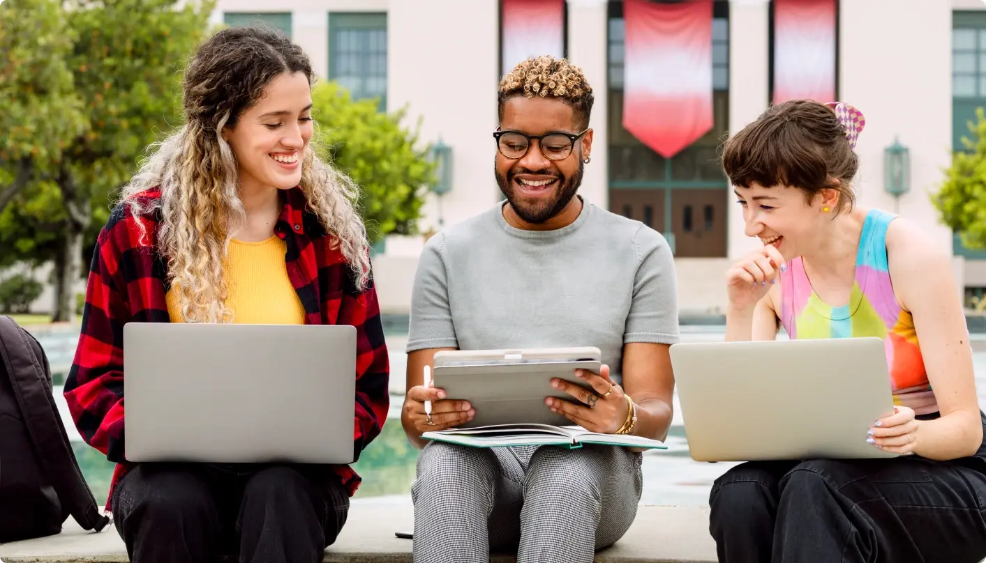 Three students smiling behind laptops about student life communications