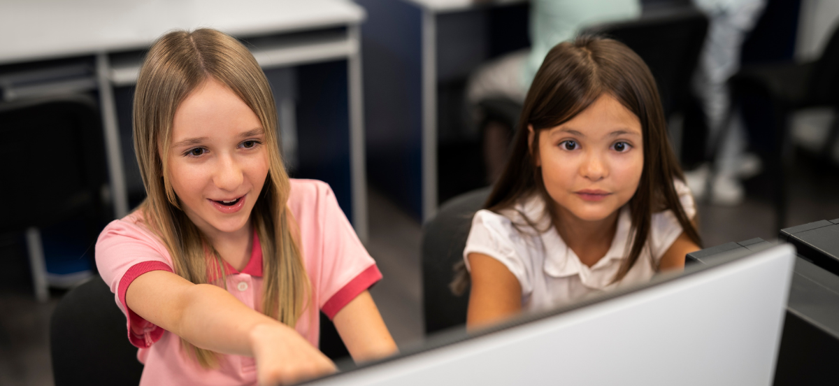 Two female students engaging in a lesson enthusiastically on a computer.