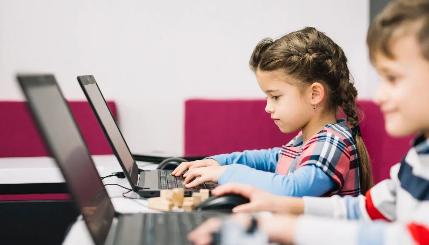 Young girl engaging in a project on her computer next to a classmate