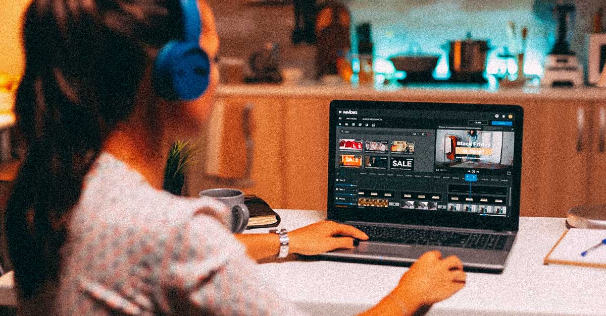 Woman sitting at laptop with headphones trimming video clips in WeVideo