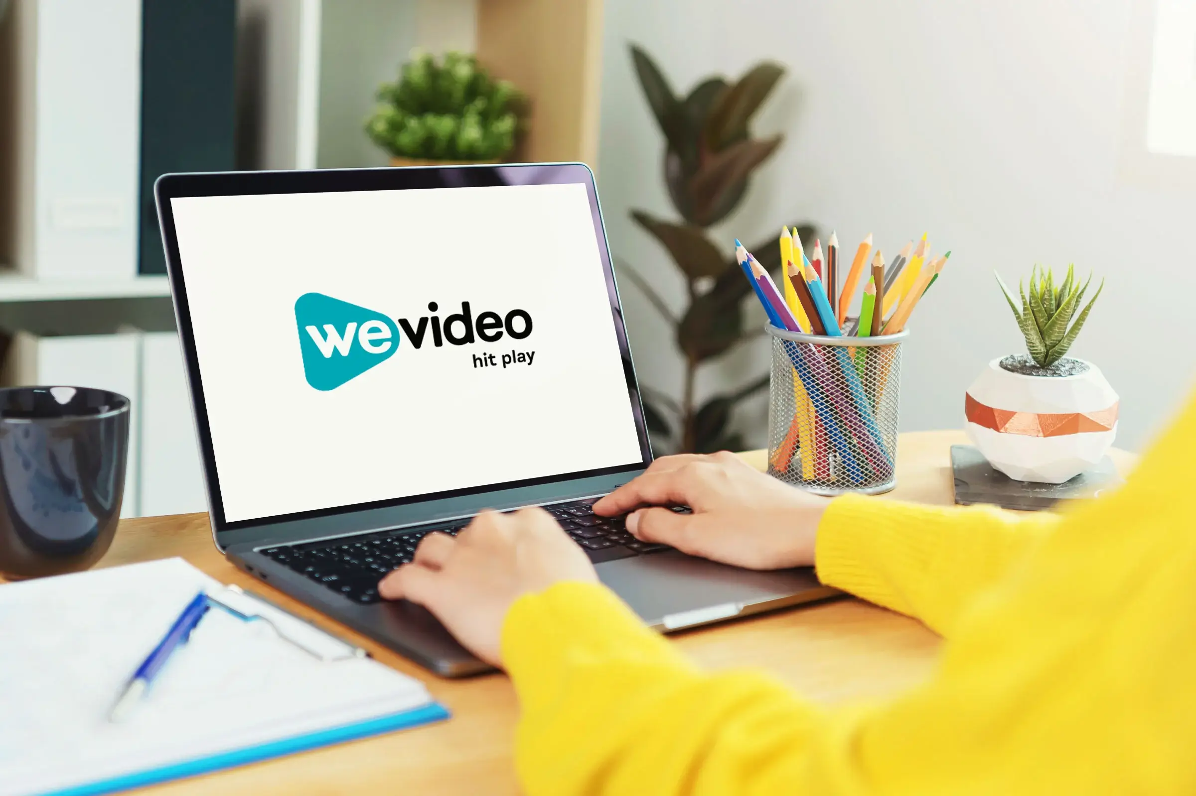 Person in yellow sweater sitting at desk with open laptop. WeVideo logo on screen.