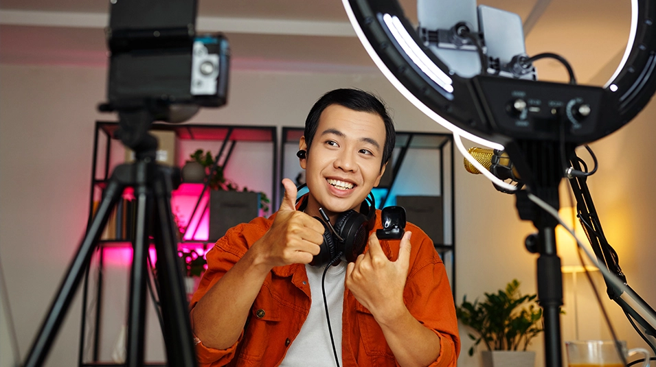 Man in front of camera tripod and ring light, smiling and giving thumbs up