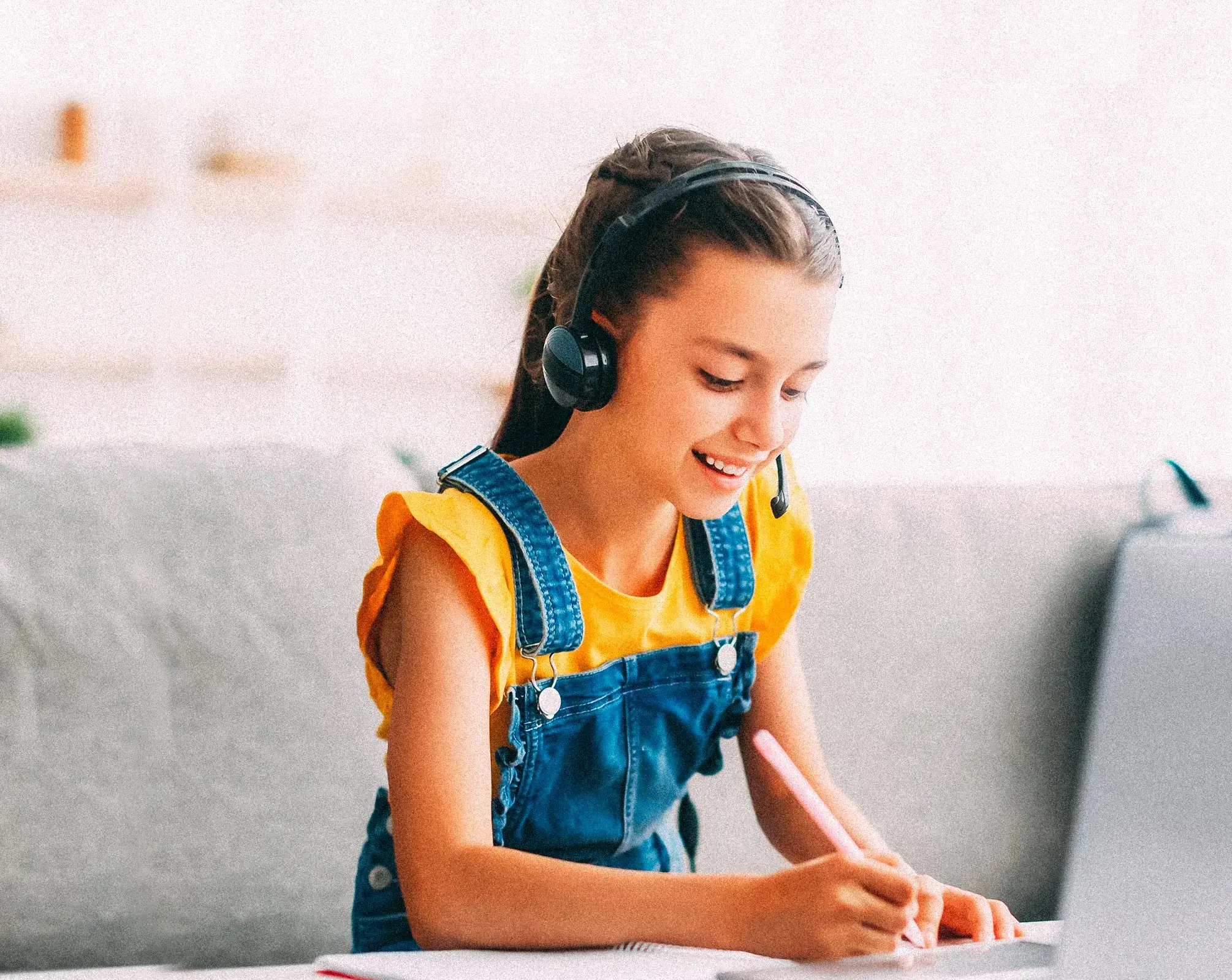 Young girl in yellow with headset on, using computer for remote learning.