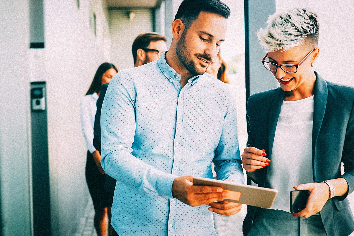 Two employees standing in an office with a tablet creating videos.
