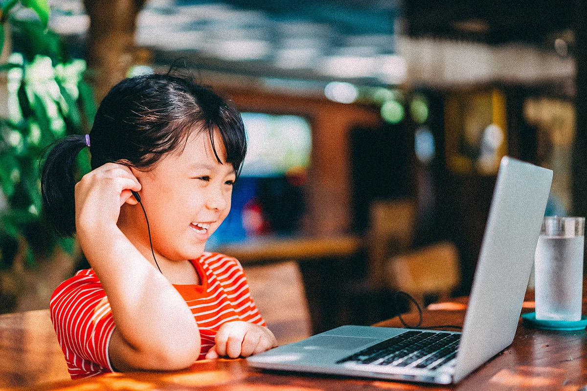 Smiling elementary-aged student listening to video on laptop.