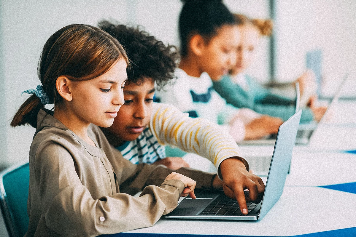 Elementary-aged children working on laptops in school.